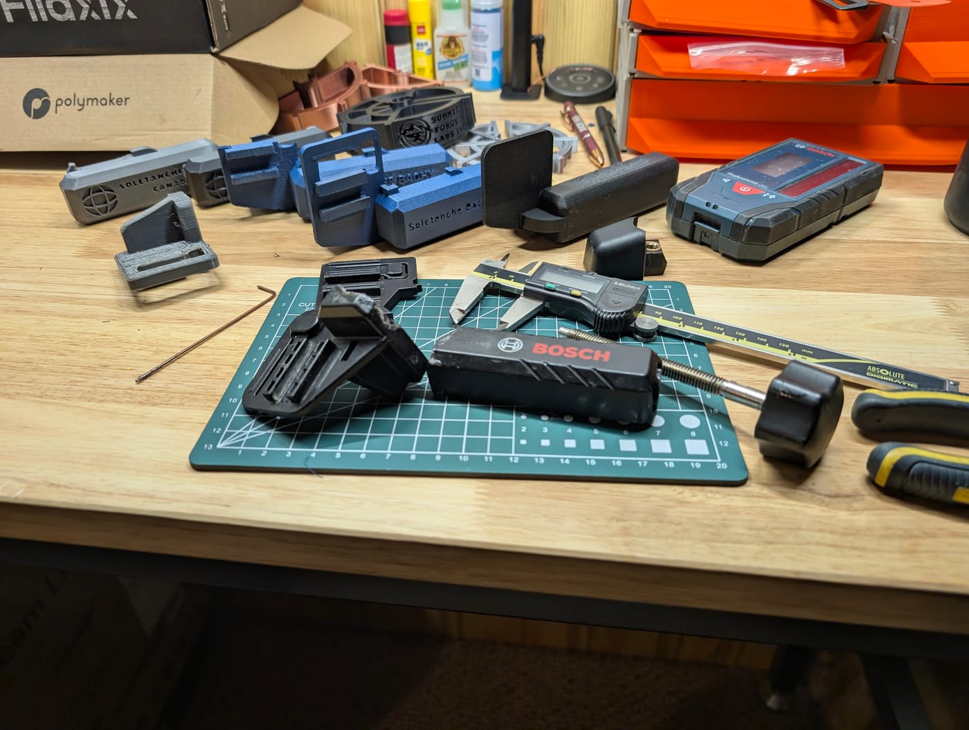 Workbench with 3D-printed brackets and fixtures, a Mitutoyo digital caliper, and Bosch measuring tools set up for reverse engineering.